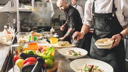 Chef et commis travaillant dans une cuisine d'un restaurant montrant les légumes et assiettes en préparation