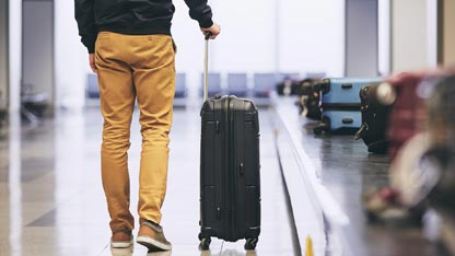 homme de dos poussant une valise dans un aéroport au niveau des tapis roulants